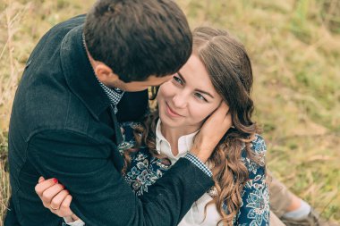 Bir adam ve bir kadın çimlerin üzerinde oturmuş birbirlerine sarılıyorlar. Adam siyah bir ceket giyiyor ve kadın mavi bir gömlek giyiyor. Birbirlerine eşlik etmek hoşlarına gidiyor gibi.