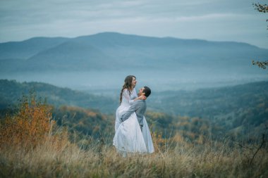 Bir çift arka planda dağlar olan bir tarlada duruyor. Kadın beyaz bir elbise giyiyor ve adam onu tutuyor. Sahne romantik ve huzurlu.