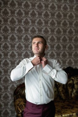 Beyaz gömlekli bir adam giyiniyor ve kravatını düzeltiyor. Görüntünün bulanık bir kalitesi var, bu da ona rüya gibi ya da gerçeküstü bir his veriyor.