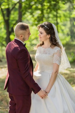 Bir gelin ve damat tarlada kameraya gülümsüyor. Gelin beyaz bir elbise ve duvak giyerken damat kırmızı bir takım elbise giyiyor. Sahne büyük ihtimalle bir düğün.