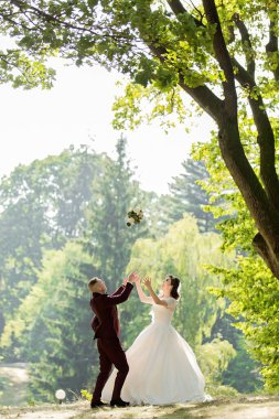 Bir gelin ve damat buketle yakalamaca oynuyorlar. Gelin beyaz bir elbise giyiyor ve damat kırmızı bir takım elbise giyiyor. Sahne arka planda ağaçlar olan bir parkta geçiyor.