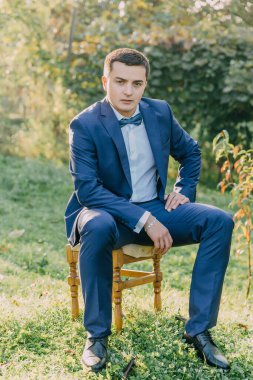 Takım elbiseli ve papyonlu bir adam çimenli bir tarlada ahşap bir sandalyede oturur. Sahne sakin ve huzur dolu. Uzağa bakan bir adam. Adamın resmi kıyafetlerinin birleşimi.