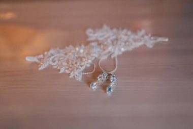 Masada bir çift küpe ve bir kolye sergilenir. Küpeler gümüş renktedir ve bir çiçek tasarımına sahiptir, kolye de gümüş renktedir ve bir çiçek tasarımına sahiptir. Masa tahtadan yapılmıştır.