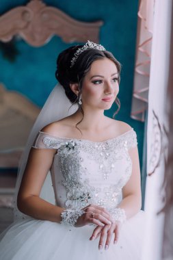 Gelinlikli bir kadın pencerenin önünde oturuyor. Bir taç ve duvak takıyor.