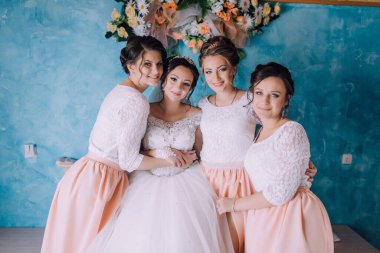 Bir grup kadın bir fotoğraf için poz veriyor, içlerinden biri gelinlik giyiyor. Sahne mutlu ve kutlama dolu, çünkü kadınlar özel bir durum için birlikte poz veriyorlar.