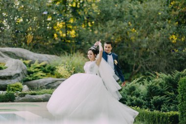 Bir gelin ve damat bahçede dans ediyor. Gelin beyaz bir elbise giyiyor ve damat mavi bir takım giyiyor.