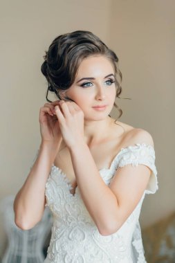 Bir kadın kulaklarını deldiriyor. O, beyaz bir elbise giyiyor. Fotoğraf bulanık ve bulanık görünüyor.