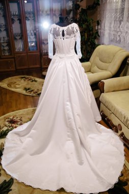 Beyaz bir gelinlik kanepenin önündeki bir halıda sergileniyor. Elbise uzun ve dantel tasarımı var.