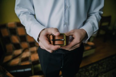 Bir adam elinde kahverengi bir kemer tutuyor. Kemer deriden yapılmıştır ve siyah bir tokası vardır. Adam beyaz gömlek ve siyah pantolon giyiyor. Formalite ve incelik kavramı