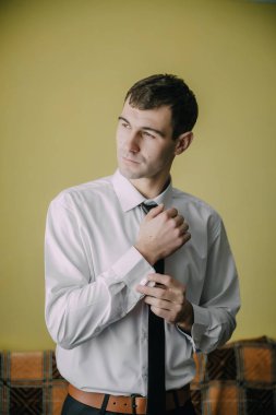 Beyaz gömlekli ve siyah kravatlı bir adam kravatını düzeltiyor. Odaklanmış ve kararlı görünüyor.