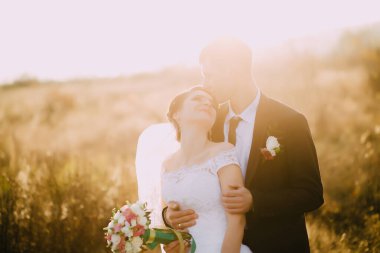 Gelin ve damat bir tarlada duruyorlar, gelin bir buket tutuyor ve damat da onu tutuyor. Çiftler düğünlerini kutlarken sahne romantik ve mutlu.
