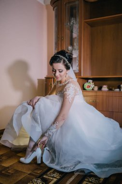 Bir gelin düğün için hazırlanıyor ve düğün ayakkabılarını giyiyor. Yerde oturuyor ve rahatlamış ve odaklanmış bir ruh hali içinde.