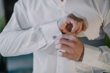 Bir adam beyaz gömlek giyiyor ve bir kelepçe takıyor. Temiz ve düzenli olduğundan emin olmak için kelepçeyi ayarlıyor.