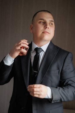 Takım elbiseli bir adam kolonya sürüyor. Siyah bir kravat ve siyah bir ceket giyiyor.