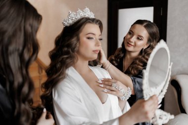 Bir kadın saçını başka bir kadına yaptırıyor. Diğer kadın bir ayna tutuyor ve kadına saçı için yardım ediyor.