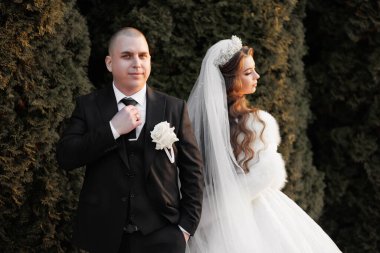 Bir erkek ve bir kadın resmi giysiler içinde yan yana duruyorlar. Adam kravat takıyor ve kadın beyaz bir elbise giyiyor. Resim için poz veriyorlar.