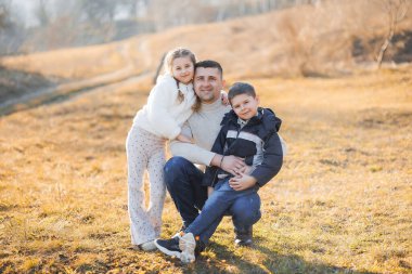 Bir adam ve iki çocuk bir tarlada fotoğraf için poz veriyorlar. Sahne sıcak ve aile odaklı.