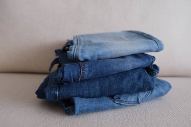 Kot pantolon, dört katlanmış ve üst üste dizilmiş kot pantolon beyaz kanepe, kot kumaş konsept fotoğraf.