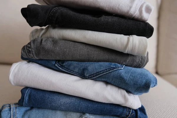 Denim pants, folded and stacked denim pants on a white sofa, denim fabric pants idea photo.