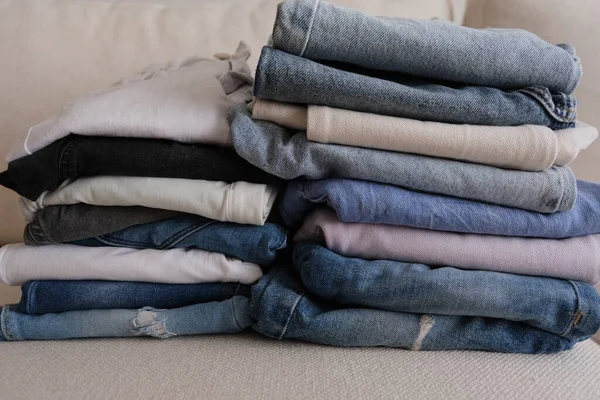 Denim pants, different colors of folded and stacked denim pants on a white sofa, denim fabric concept idea photo.