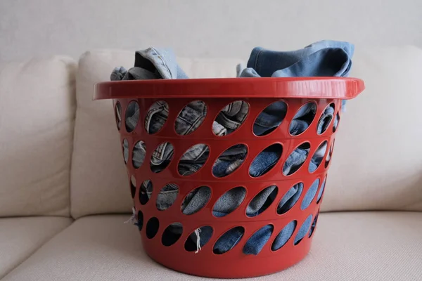 Kot pantolon, beyaz bir kanepede kırmızı bir sepette açık kot pantolon. Dağınık kot pantolon konsepti fikri fotoğrafı. Kırmızı bir sepetin ön görüntüsü. 