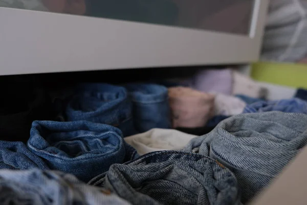 Drawer stack of denim clothes, fully open white drawer stack of folded denim jeans clothes indoors, close up. Selective focus. Denim concept idea photo.