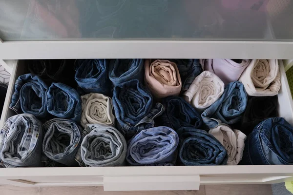 Drawer full of denim clothes, neatly folded denim jeans clothes are vertically in the white chest of drawers. Denim storage concept idea photo.