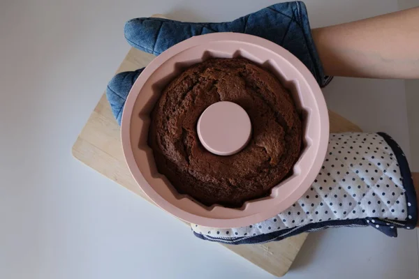 Baked cake in a silicone mold, A woman puts a cacao cake in a pink round silicone mold on a wooden cutting board in the kitchen. The concept photo of homemade food.