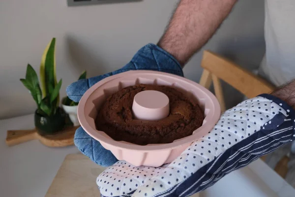 Baked cake in a silicone mold, A man puts a cacao cake in a pink round silicone mold on a wooden cutting board in the kitchen. Cacao cake concept photo idea.