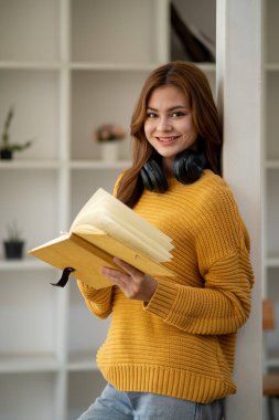 Güzel, gülümseyen, kulaklık takan, elinde kitap tutan bir öğrenci kız öğrenci portresi kafa ve el dengeleyici kitaplar taşıyor.