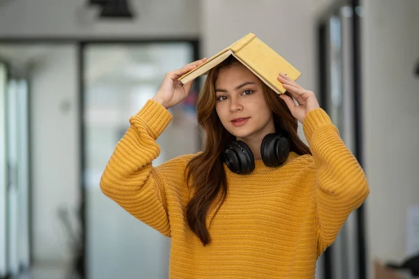 Güzel, gülümseyen, kulaklık takan, elinde kitap tutan bir öğrenci kız öğrenci portresi kafa ve el dengeleyici kitaplar taşıyor.
