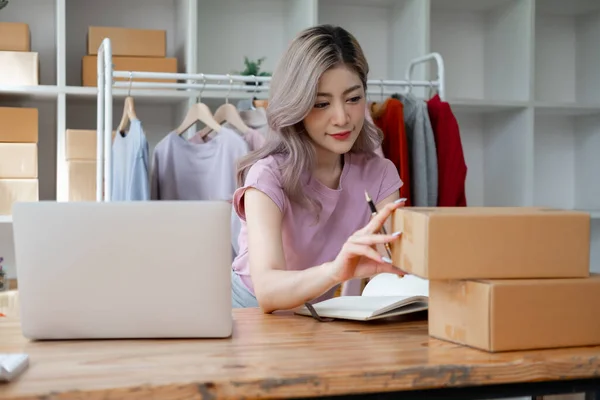 Young woman owner ship business start small business in a cardboard box and calculate price product by calculator and laptop computer
