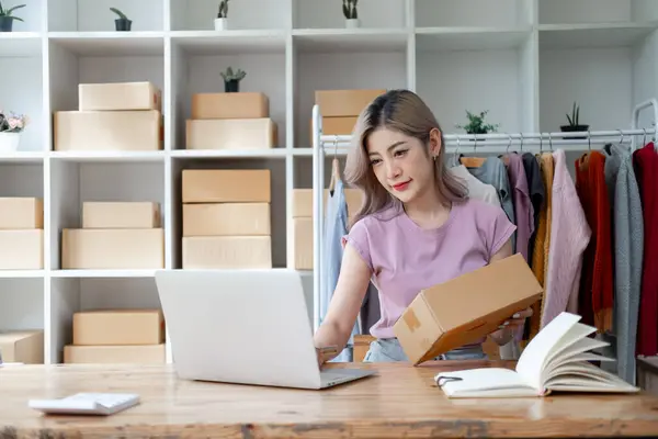 Young woman owner ship business start small business in a cardboard box and calculate price product by calculator and laptop computer