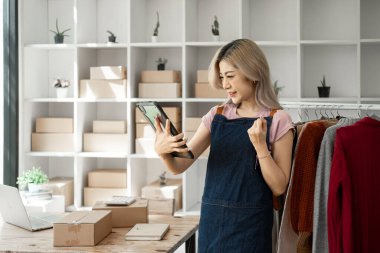 Genç, mutlu kadın moda blogcusu kadın işyeri sahibi günümüze uygun çek kıyafetlerini gösteriyor ve canlı internet dükkanında satıyor. 
