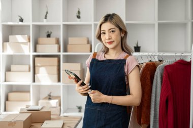 Genç, mutlu kadın moda blogcusu kadın işyeri sahibi günümüze uygun çek kıyafetlerini gösteriyor ve canlı internet dükkanında satıyor. 
