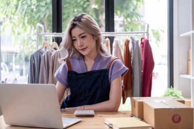 Genç, mutlu kadın moda blogcusu kadın işyeri sahibi günümüze uygun çek kıyafetlerini gösteriyor ve canlı internet dükkanında satıyor. 