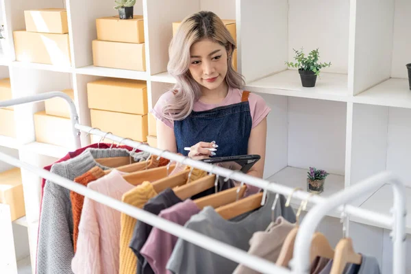 Genç, mutlu kadın moda blogcusu kadın işyeri sahibi günümüze uygun çek kıyafetlerini gösteriyor ve canlı internet dükkanında satıyor. 