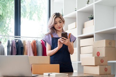 İş kadını sahibi cep telefonlu cep telefonu sahibi müşteriyle sohbet etmek için cep telefonu kullanıyor. Telefon ve perakende ürün taşıyan küçük işletme sahibi teslimat için hazırlanıyor.