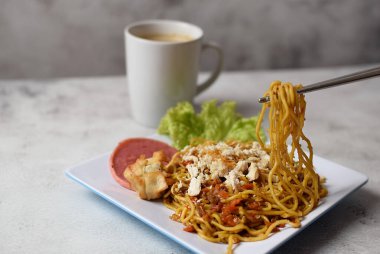 Mie Goreng, baharatlı kızarmış şehriye, tavuklu ve biberli. Yanında da bir fincan kahve ve sebze ve gri arka planda servis ediliyor.