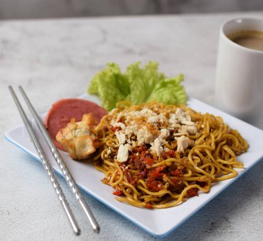 Mie Goreng, baharatlı kızarmış şehriye, tavuklu ve biberli. Yanında da bir fincan kahve ve sebze ve gri arka planda servis ediliyor.