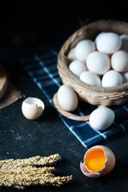 taşralı tavuk yumurtaları ya da evcil tavuk yumurtaları ya da serbest tavuk yumurtaları (telur ayam kampung). Sepet ve kumaş üzerine kurulmuş koyu renk ve dokuma arka planda. Bir yumurta kırıldı.