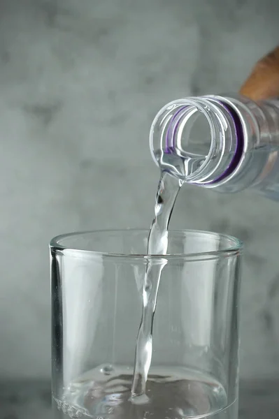 Tangan Menuangkan Air Dari Botol Kaca Pada Latar Belakang Abu — Stok Foto