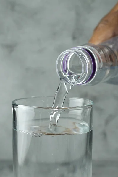 在灰色和纹理背景下 将水从瓶子倒入玻璃杯中 — 图库照片