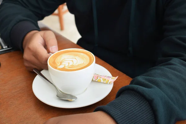 Pria Tangan Dalam Sweater Biru Memegang Cangkir Cappuccino Atas Meja — Stok Foto