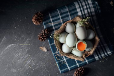 Bambu sepetinde taze çiğ ördek yumurtası ve koyu renk ve dokuma arka planda çuval bezi. Bir yumurta kırıldı. Yumurta sarısı tuzlu ördek