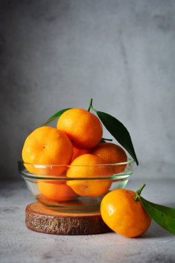 Cam bir kasede bir sürü portakal meyvesi. Gri ve doku arka planında mandalina portakalı meyveleri 