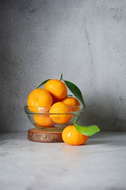Cam bir kasede bir sürü portakal meyvesi. Gri ve doku arka planında mandalina portakalı meyveleri 