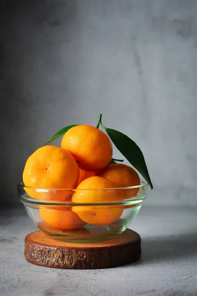 ガラスボウルに オレンジ色の果物がたくさんあります グレーとテクスチャの背景にマンダリンオレンジのフルーツ ストックフォト