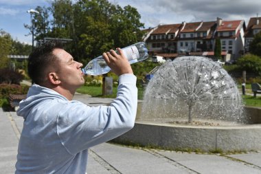 Yazın su içen bir adam ve arka planda bir çeşme.