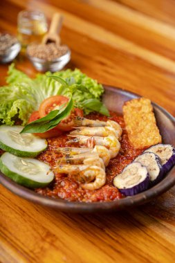 Baharatlı biber soslu karides ya da ahşap masadaki çömlek tabağında sambal ve patlıcan.